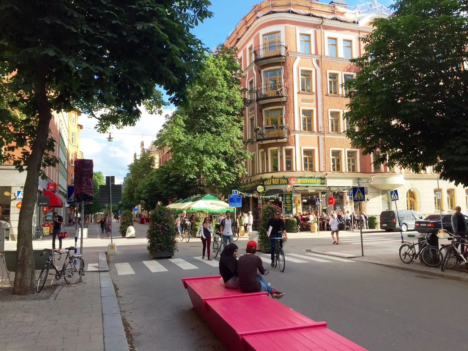 People sitting on a red bench at a lively crossing on a car-free street in summer.