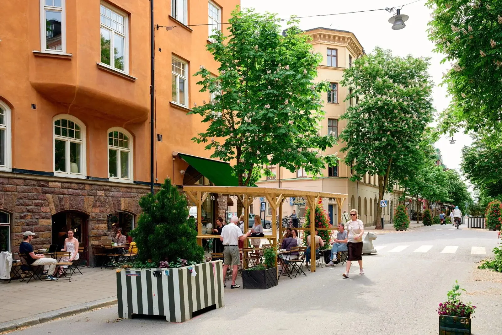Outdoor café seating under blossoming chestnut trees on a car-free summer street in Stockholm, people sitting at tables out in the street.